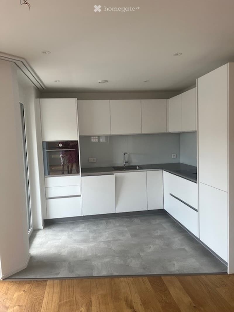 Modern kitchen with white cabinets, a sink, and an oven. The floor is a combination of grey tiles and wooden planks.