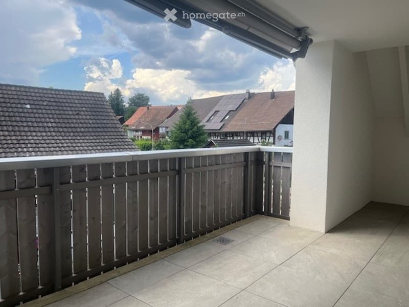 Balcony with wooden railing, tiled floor, and a view of neighboring houses and trees.
