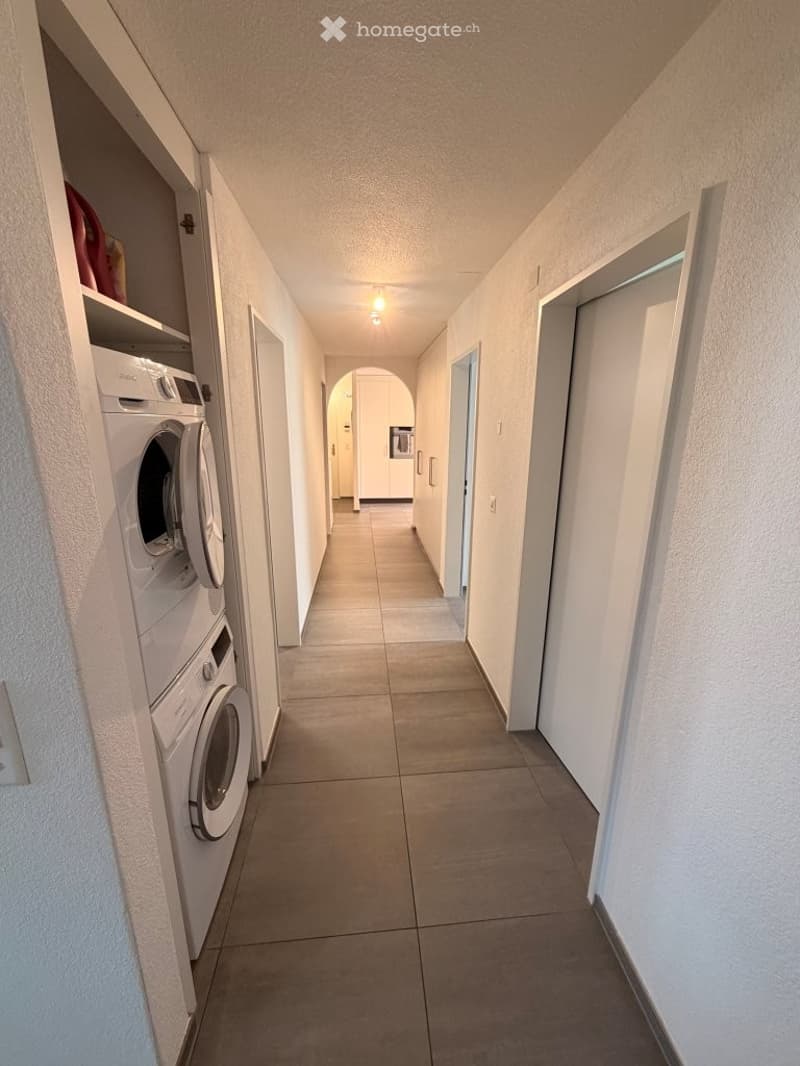 Clean, well-lit hallway with tiled flooring, white walls, and built-in washing machines on one side.