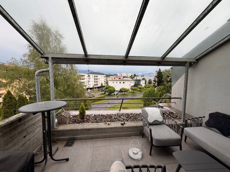 Balcony with a view of the city, featuring a round table, chairs, and a small sofa.