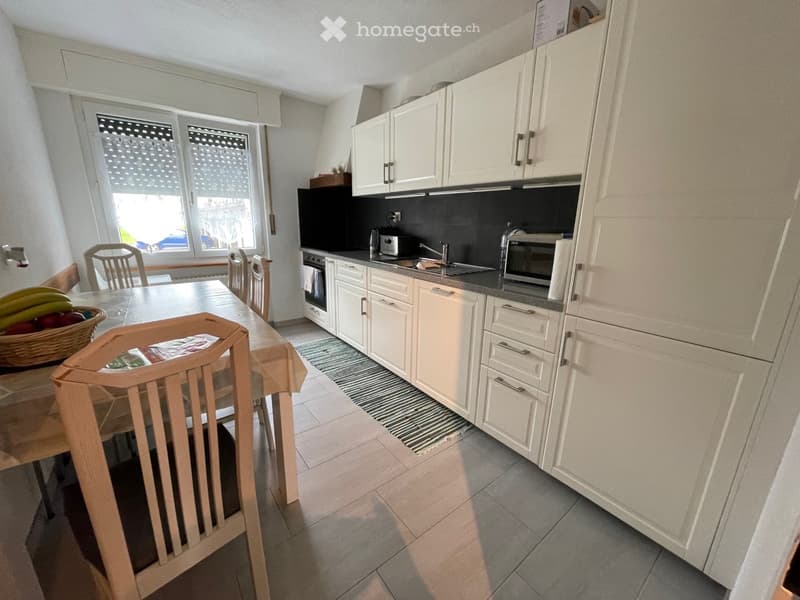 Modern kitchen, white cabinets, black countertops, tiled floor, dining table, chairs, breakfast items