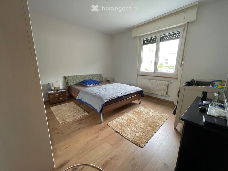 A bedroom with a bed, nightstands, rugs, and a window.