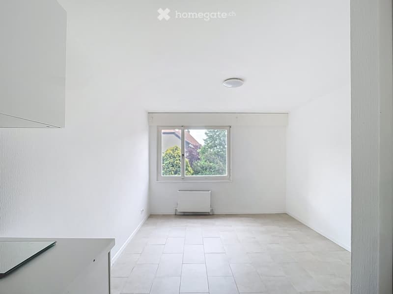 Empty room with white walls, tiled floor, a single window, and a radiator below it.