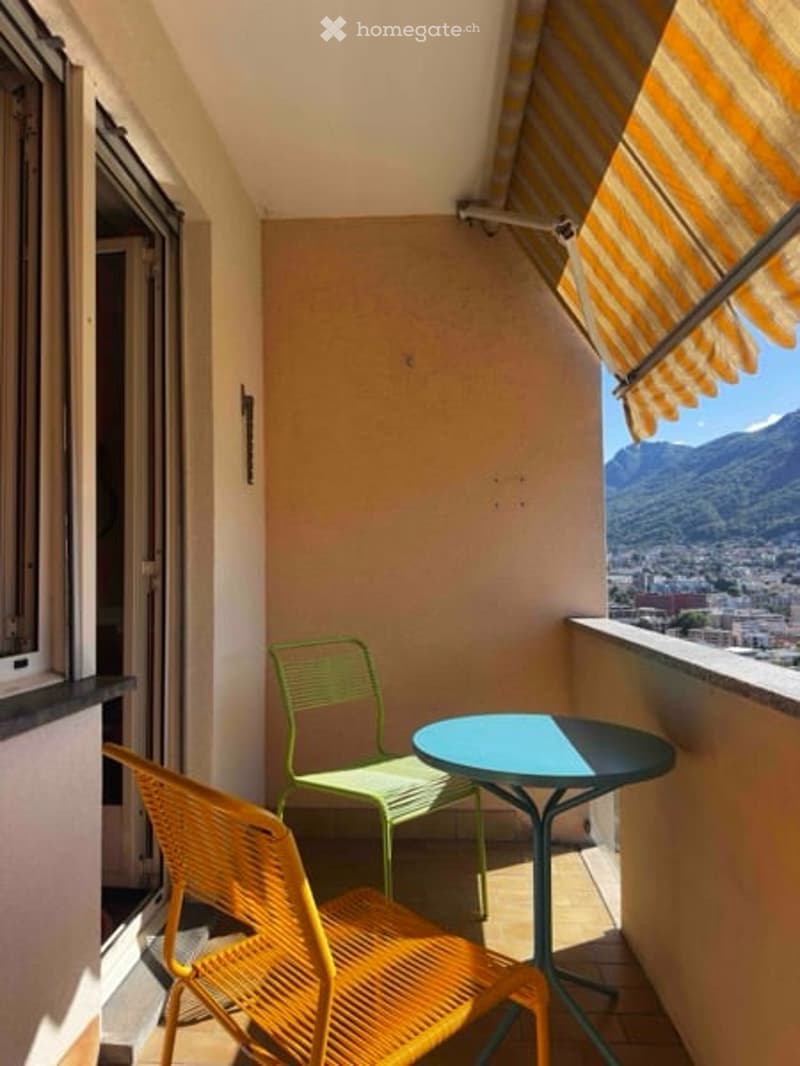 Balcony with a view of the city and mountains, equipped with a small table and two chairs.