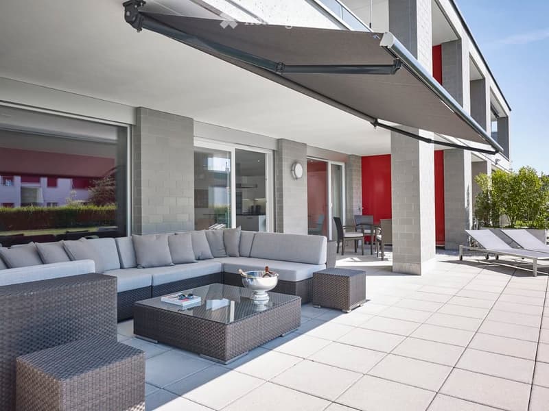 Modern outdoor patio with a large sectional sofa, coffee table, and lounge chairs under a retractable awning.