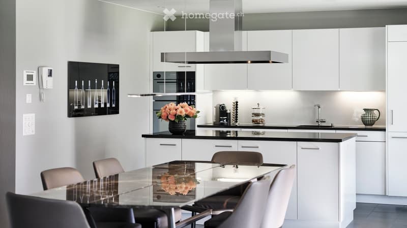 Modern kitchen with white cabinets, stainless steel appliances, a glass dining table with chairs, and a vase of flowers on the counter.