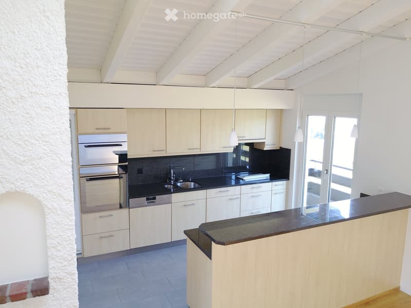 Modern kitchen with light wood cabinets, stainless steel appliances, black countertops, and a central island.