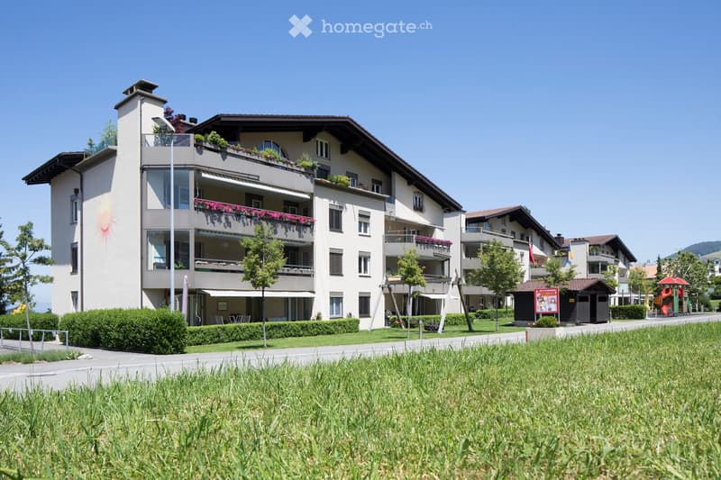 Multi-story residential building with balconies, greenery, and a well-maintained lawn in front.