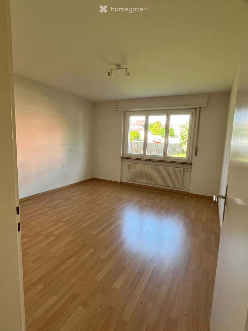 Empty room with wooden flooring, white walls, and a large window with a radiator below it.