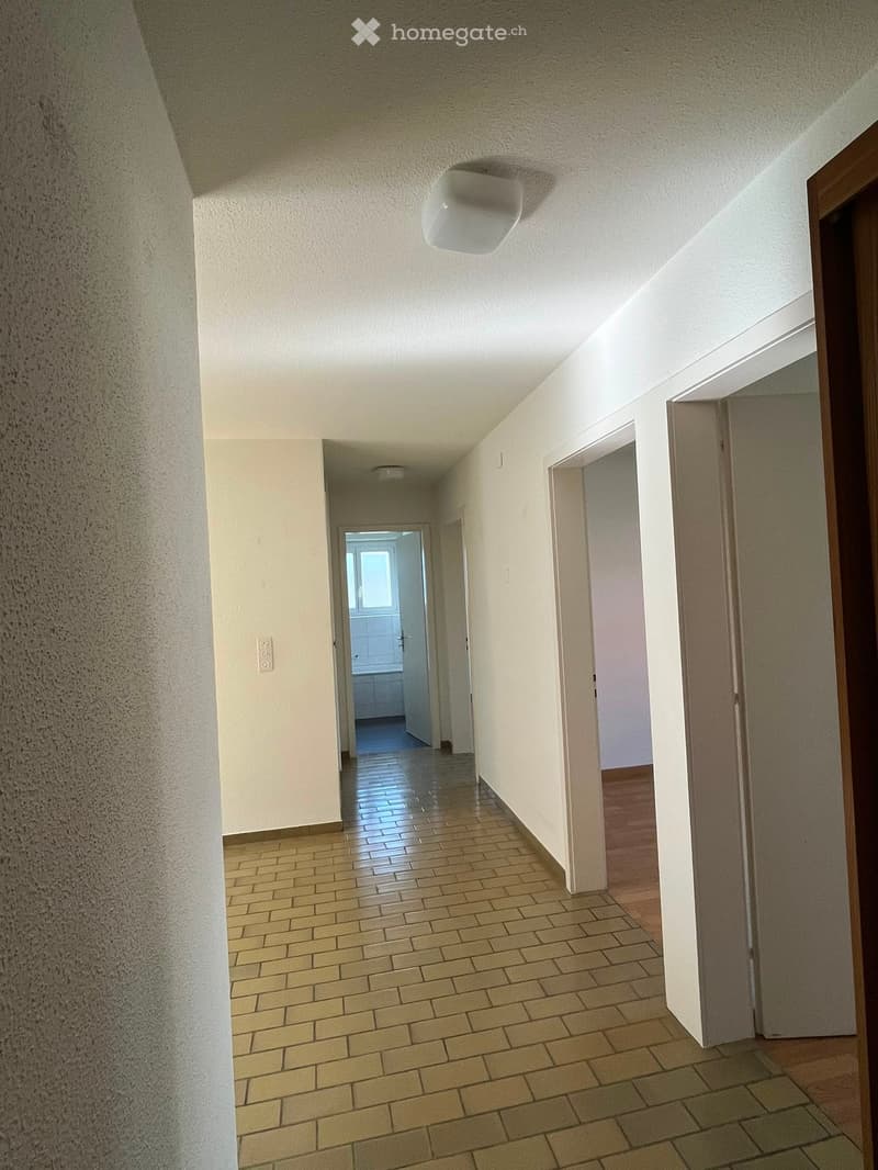 Empty hallway with tiled floor, white walls, and several doors leading to other rooms.