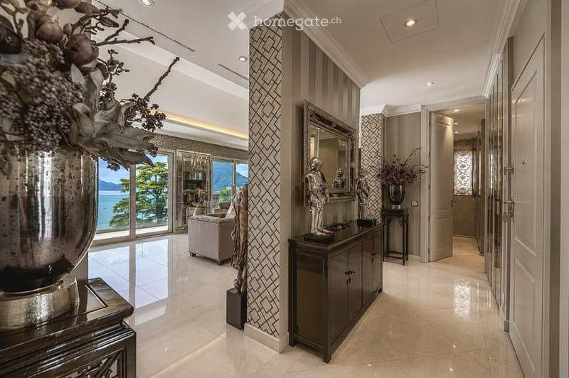 Elegant hallway with patterned wall design, large mirrors, decorative statues, and a view of the ocean through large windows.