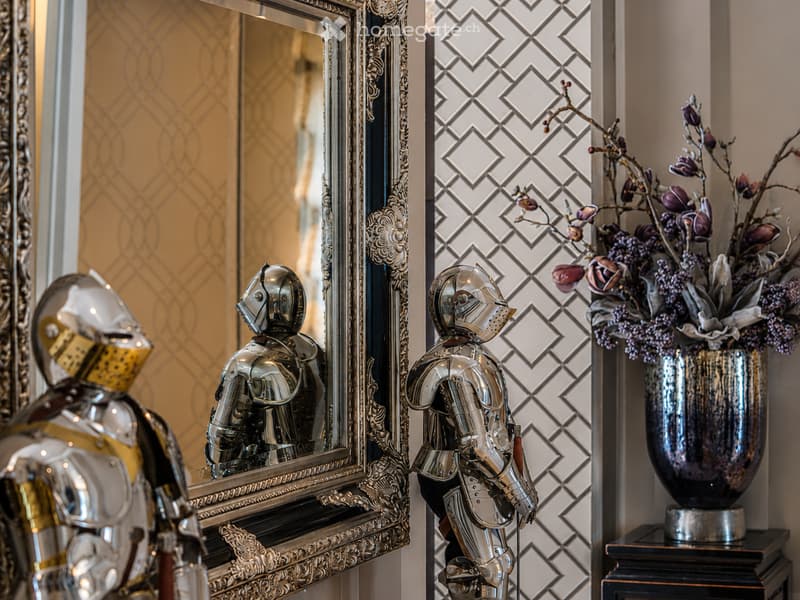 Elegant room with ornate mirror, silver knight statue, and decorative vase with flowers on a small table.