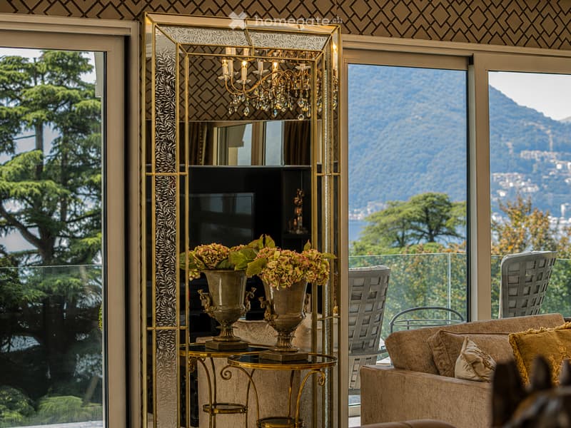 Elegant living room with large windows offering a scenic mountain view, featuring a patterned sofa, gold-framed mirror, chandelier, and decorative vases on a small table.