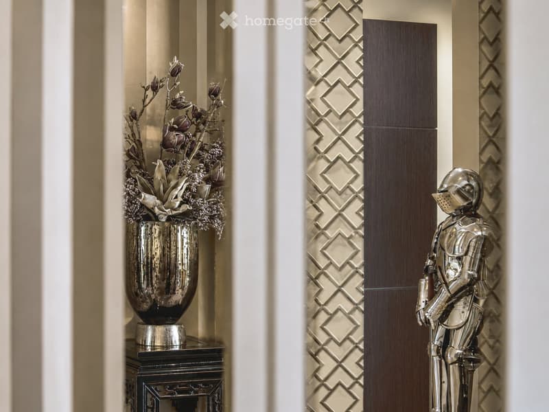 Elegant hallway with a decorative vase on a small table and a metallic knight statue near a patterned wall.