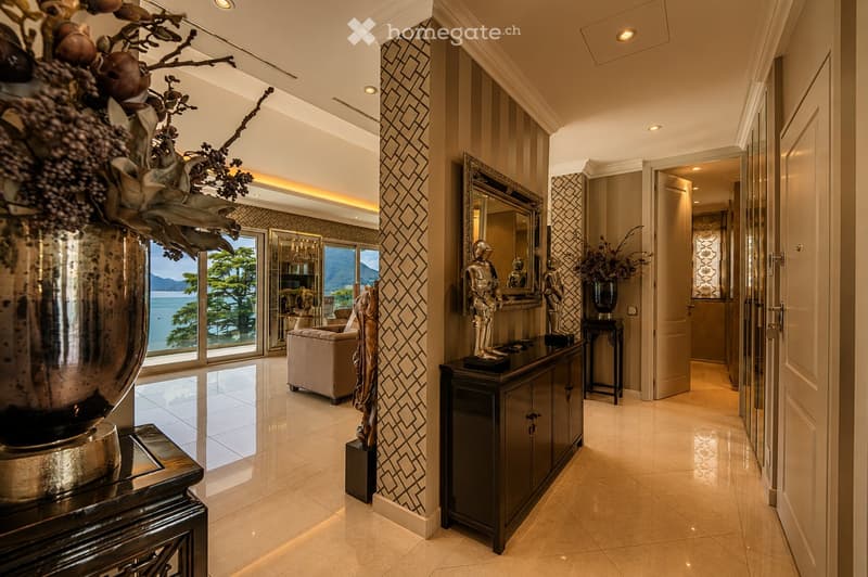 Elegant hallway with patterned wall design, large mirrors, decorative statues, and a view of the ocean through large windows.