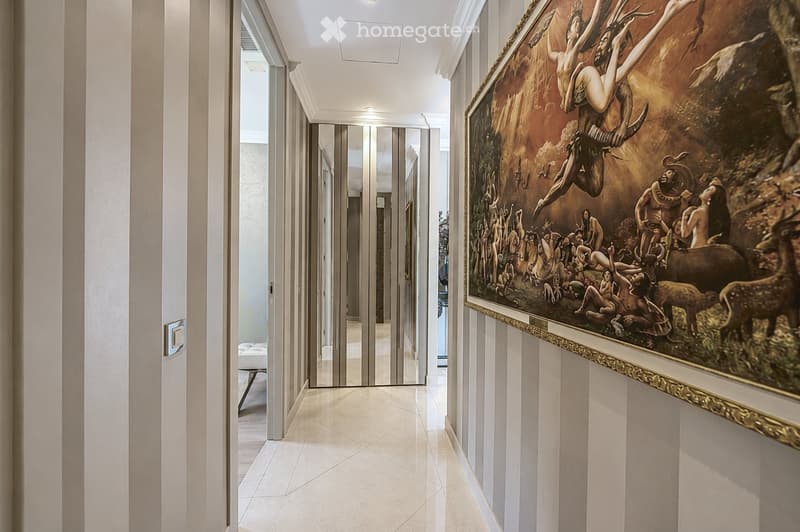 Elegant hallway with white walls, polished tile flooring, large framed artwork, and a view into an adjacent room with a bed and nightstand.