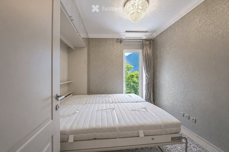 Cozy bedroom with two single beds, patterned wallpaper, large window with a scenic mountain view, and a chandelier.