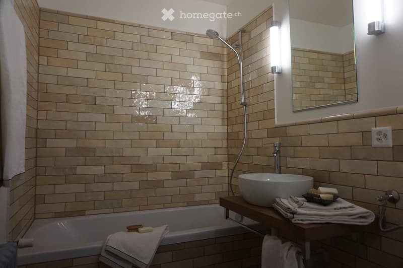 Bathroom. Modern bathroom with beige tiled walls, a bathtub, a sink with a modern faucet, a large mirror, and neatly arranged towels and toiletries.