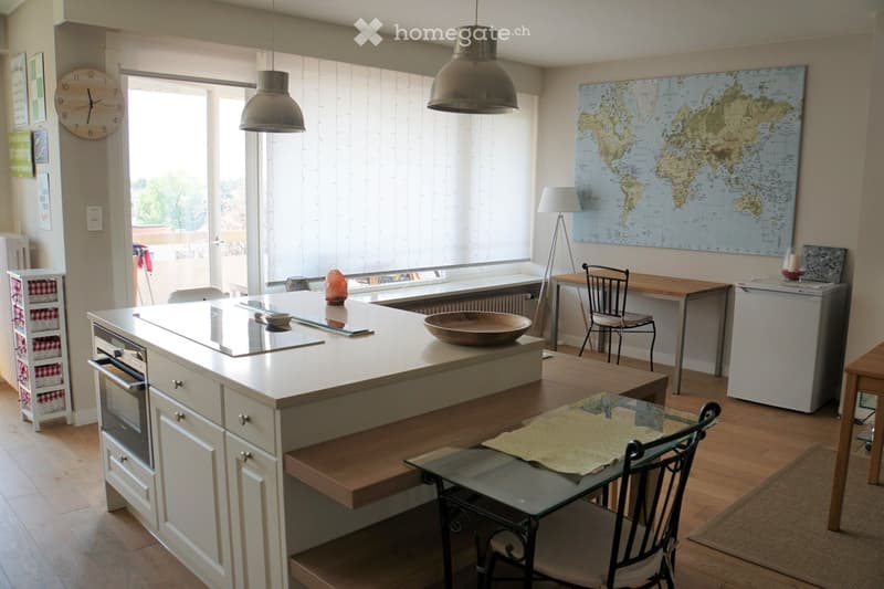 Modern kitchen with a central island, built-in oven, refrigerator, dining area with a table and chairs, and a world map on the wall.