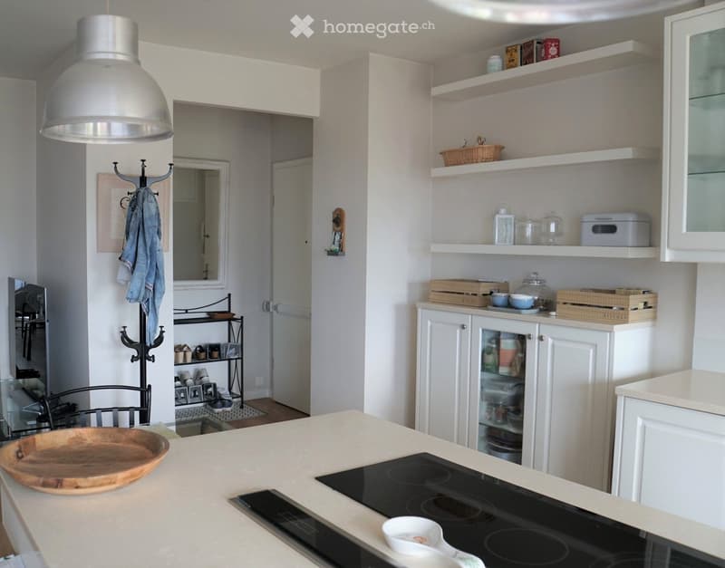 Modern kitchen with white cabinets, an induction stove, wooden bowl, and open shelving displaying various items.