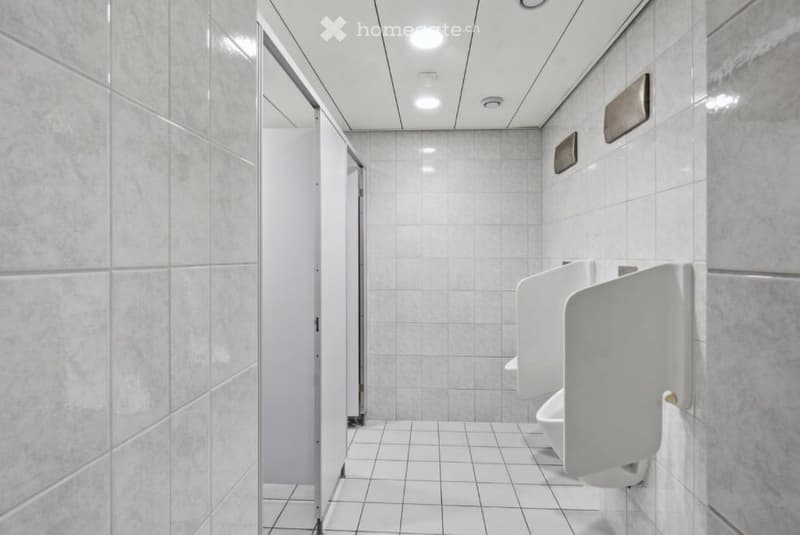 Bathroom. Modern public restroom with white tiled walls and floor, multiple urinals and a toilet stall.