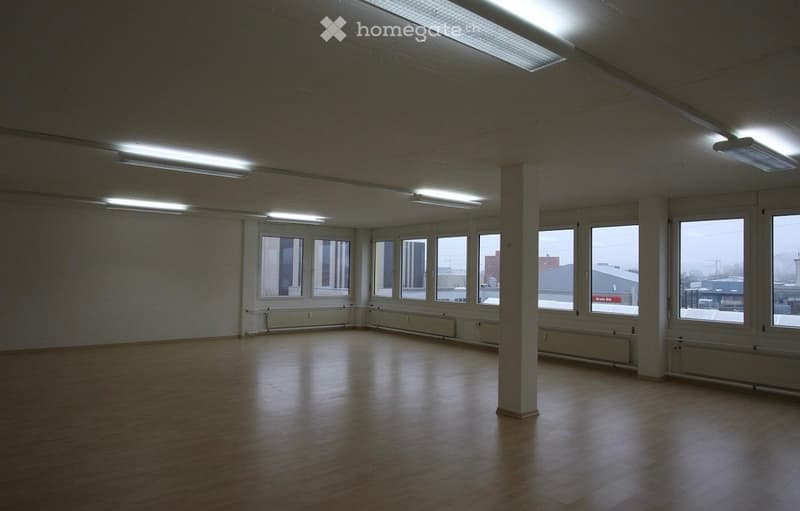 Unfurnished Room. Empty room with wooden flooring, white walls, large windows, and fluorescent lighting.
