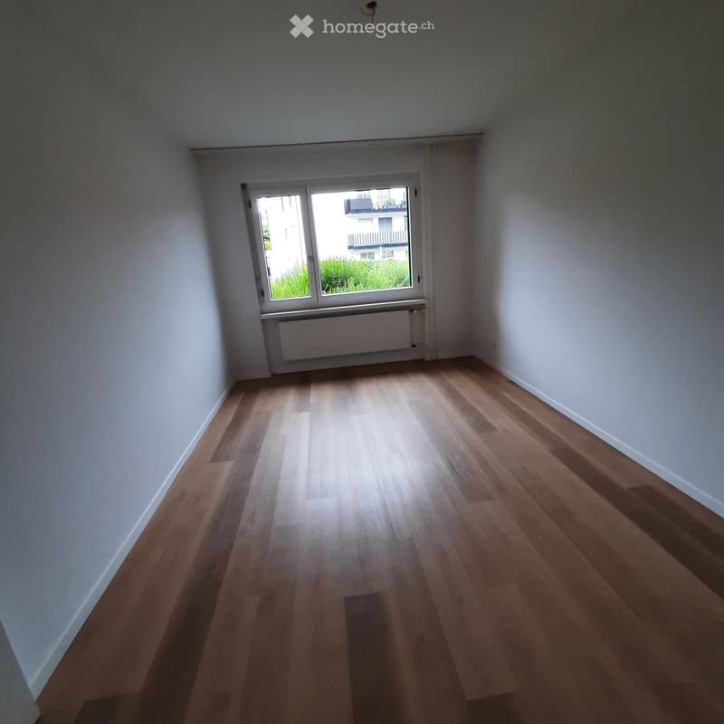 Empty room with wooden flooring, white walls, and a window with a radiator below it.