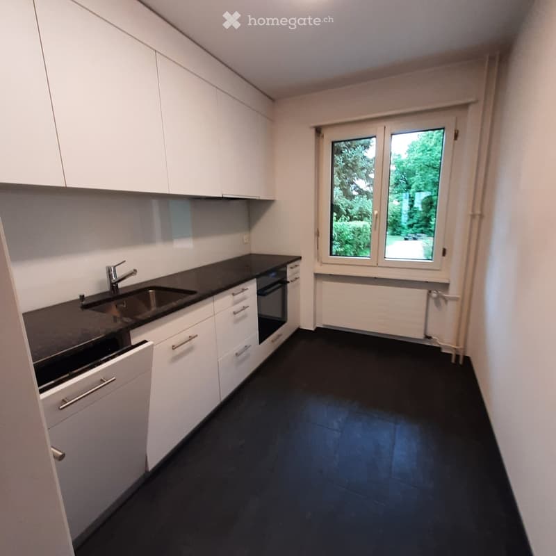 Modern kitchen with white cabinets, black countertops, and a stainless steel sink. Features an oven and ample storage space.