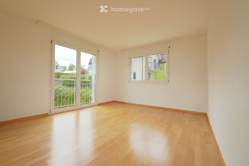 Empty room with light wooden flooring, white walls, large windows, and a sliding glass door leading to a balcony.