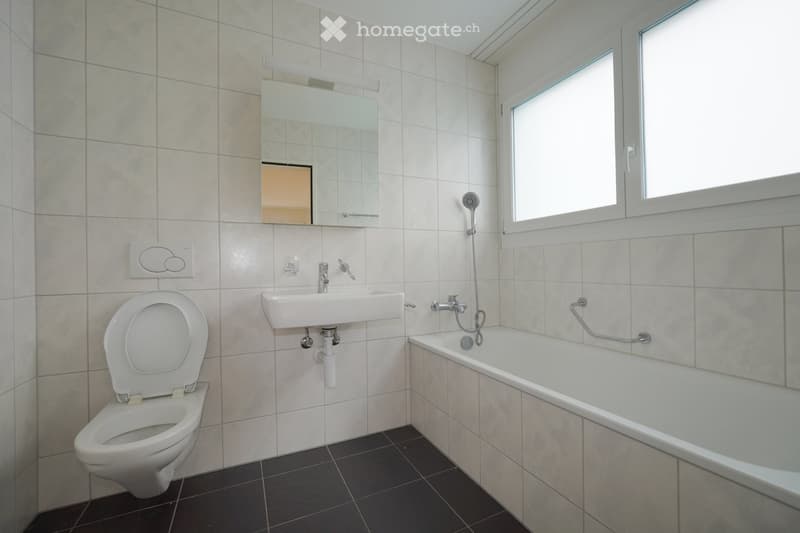 Modern bathroom with white tiles, a toilet, a sink, a bathtub, a mirror, and a showerhead.