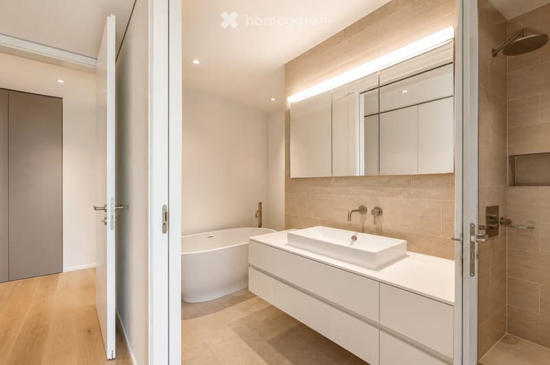 Modern bathroom with a freestanding bathtub, a white sink with a sleek faucet, a large mirror with built-in lighting, and a glass-enclosed shower area with a modern showerhead.