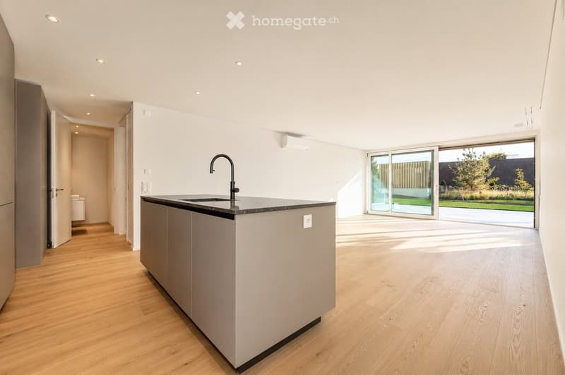 Modern kitchen with light wooden flooring, white walls, and a central island with a black countertop and sink.