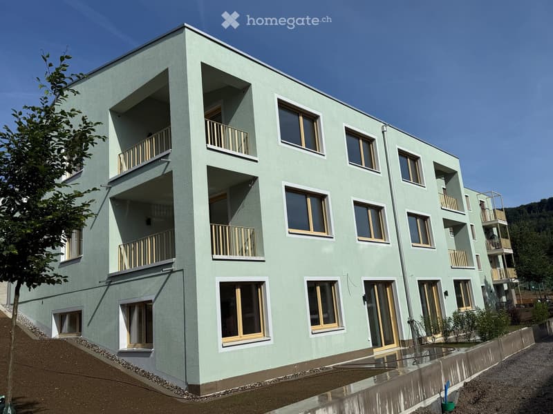 Modern multi-story building with light green facade, multiple balconies, large windows, and a raised ground floor.