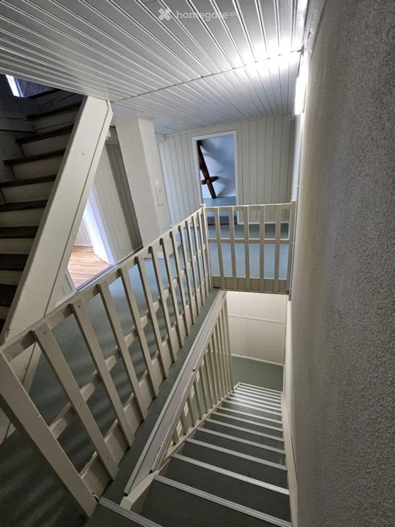 Staircase with wooden railings and carpeted steps, leading to an open area with a view of another room.