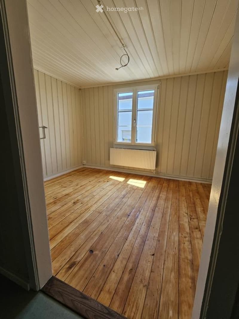Empty room with wooden flooring, paneled walls, and a single window with a radiator below it.