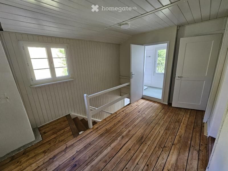 Empty wooden staircase leading up, with white railings and open door at the top, wooden floor, and white walls.