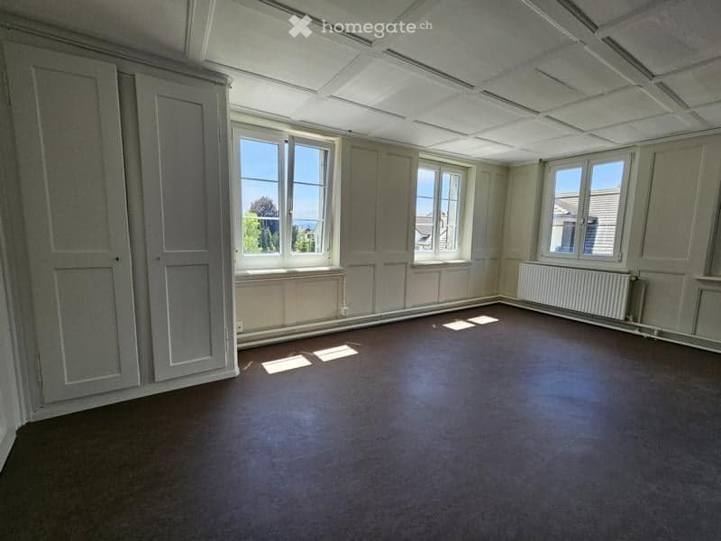 Empty room with wooden flooring, white walls, large windows, and built-in cabinets.