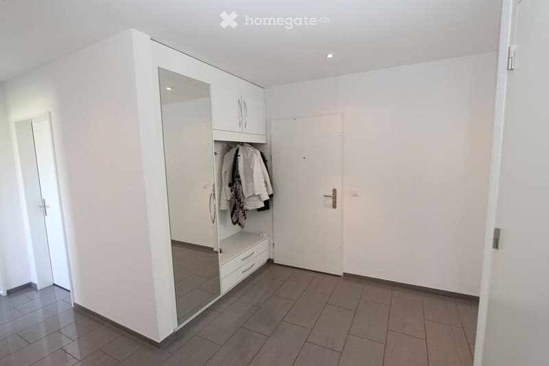 Empty hallway with white walls, tiled floor, built-in white closet with mirrored door, and a closed door at the end.