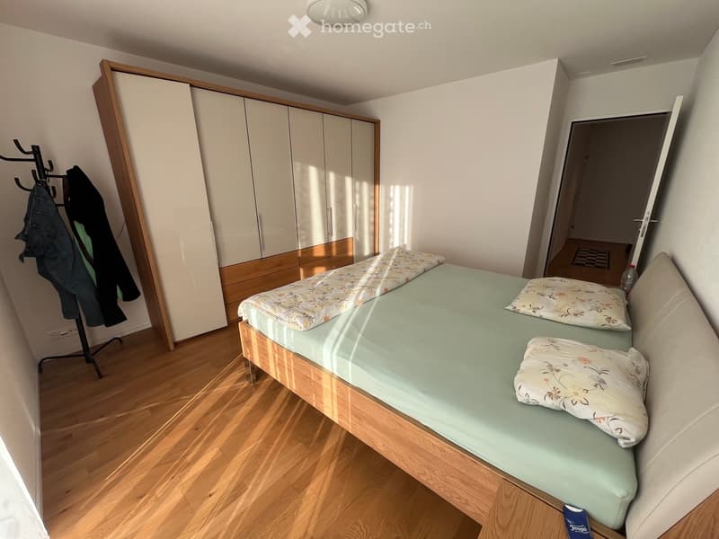 A tidy bedroom with a single bed, a wardrobe, and a coat rack. The bed has a light green mattress and floral-patterned bedding.