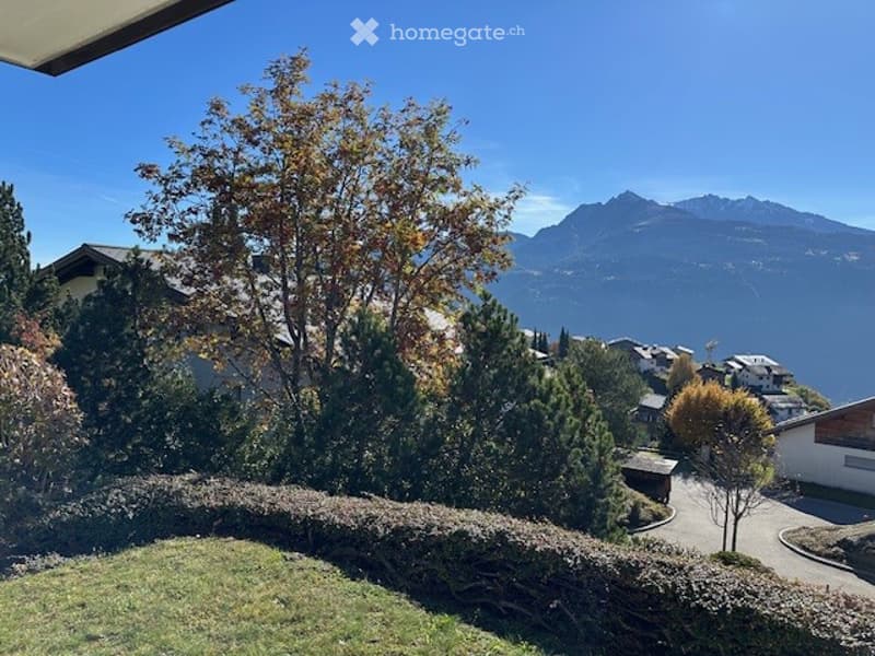 Balcony or terrace view overlooking a scenic valley with mountains, trees, and houses below.