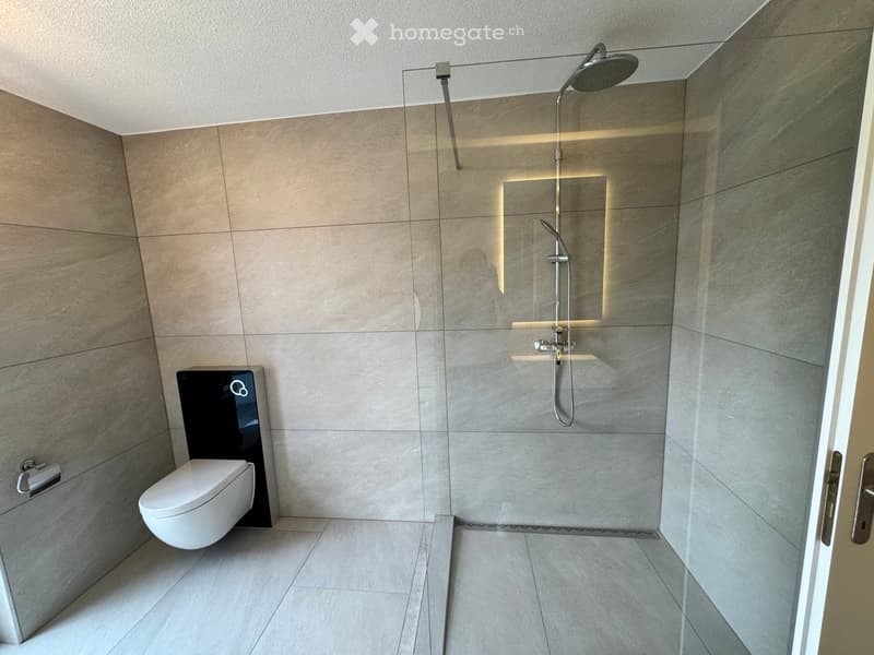 modern bathroom with walk-in shower, white toilet, tiled walls, glass door, shower head, and silver fixtures
