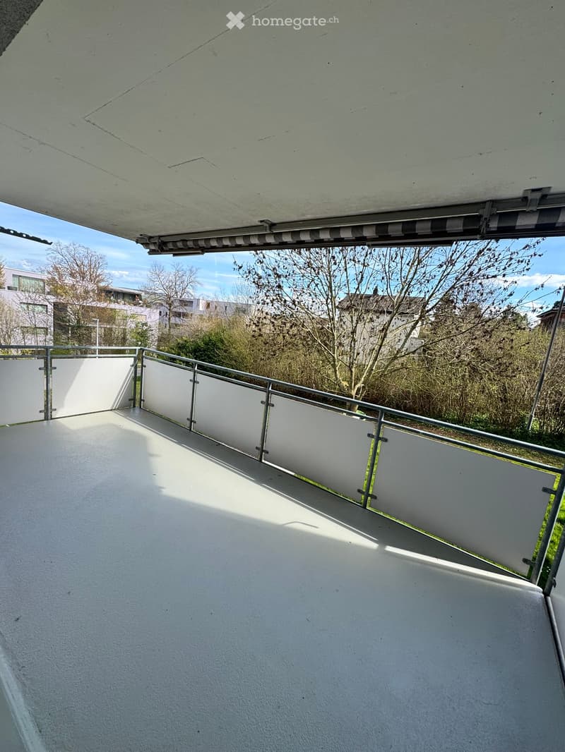 Balcony with metal railings, white walls, and a view of trees and buildings