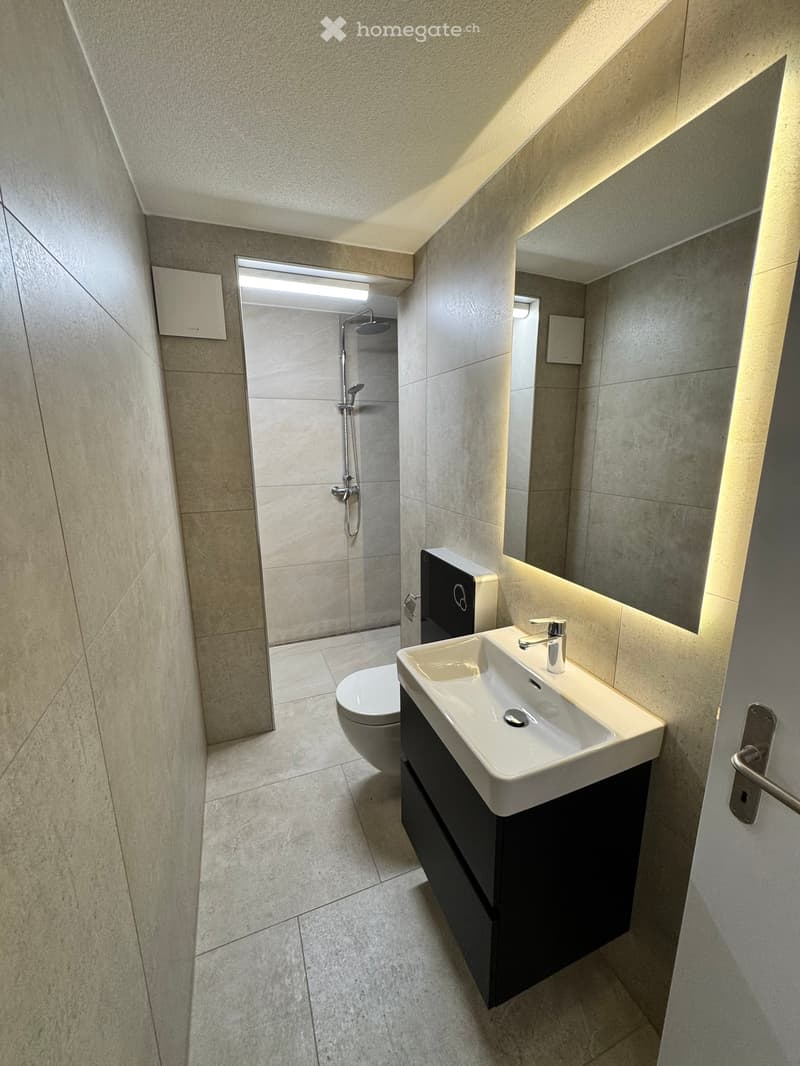 modern bathroom with white sink, black cabinet, white toilet, shower, mirror, tiled floor