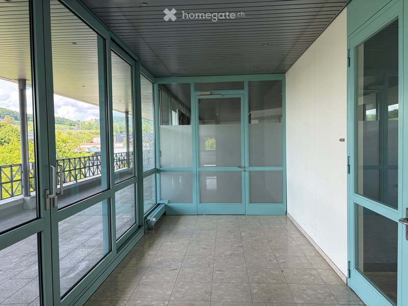 Balcony with tiled floor, glass doors, and metal railing, overlooking a green landscape.
