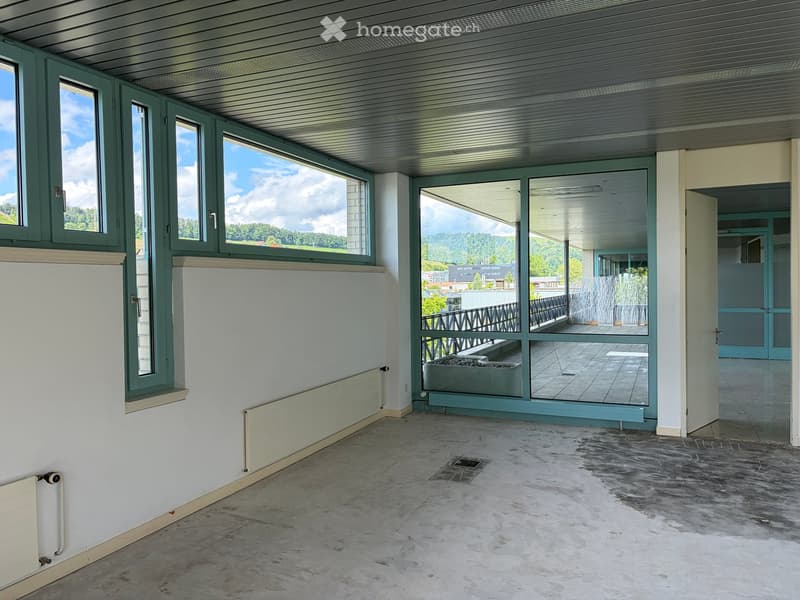 Empty room with concrete floor, white walls, large windows, and a view of the outdoor area.