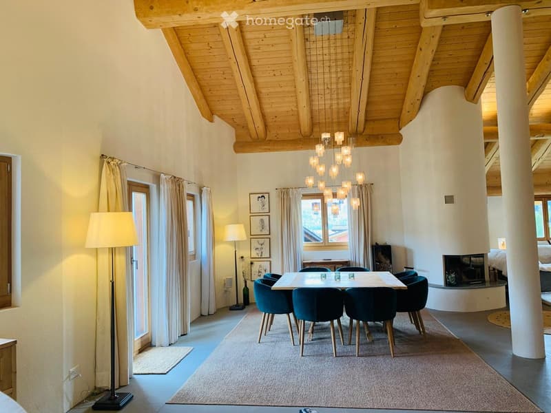 Dining area with a modern wooden ceiling, large windows, a dining table with six chairs, floor lamp, picture frames, and a fireplace in the background.