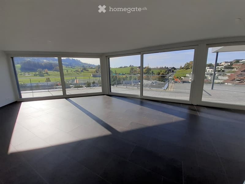 Empty room with large windows and a tiled floor, offering a scenic view of green fields and hills.