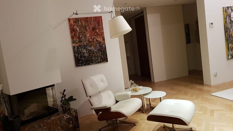Modern living room with white leather chair, ottoman, small round table, fireplace, and artwork on the wall.