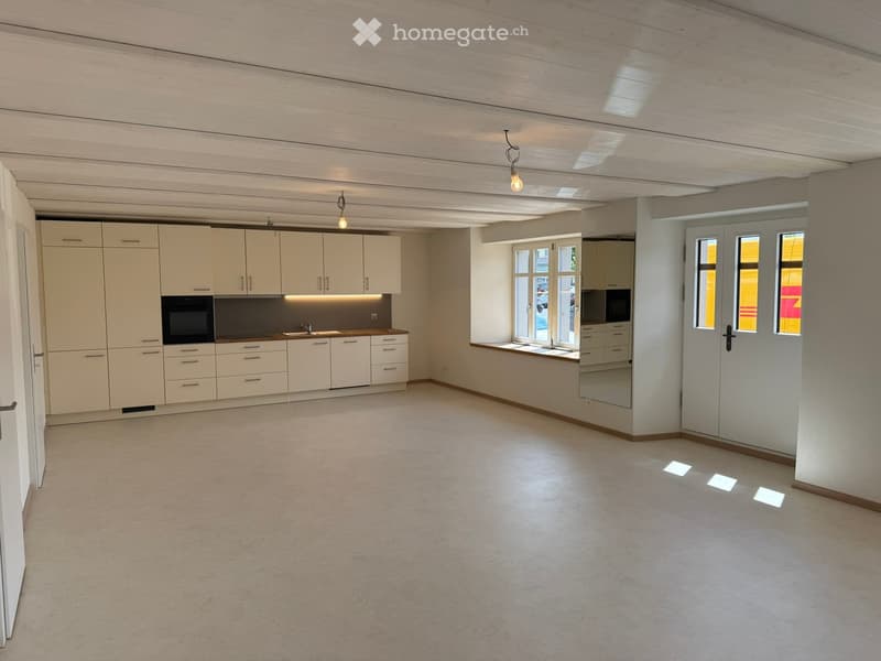 Empty room with white cabinets, sink, and windows, featuring a tiled floor and exposed wooden ceiling.