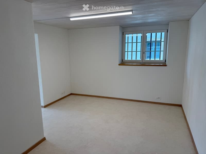 Empty room with white walls, light-colored carpet, and a single window with bars. No furniture or equipment present.